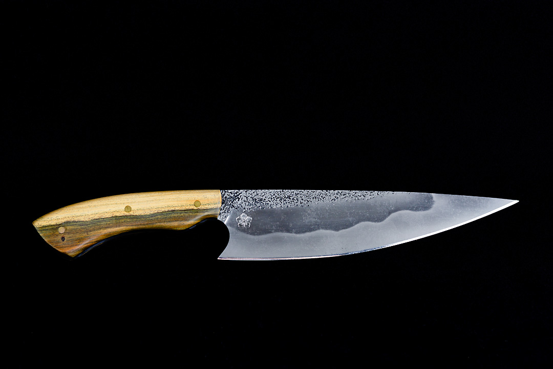 Product photography of a knife with the Kanji Knives logo ingraved on a black background. The knife has a bright brown handle.