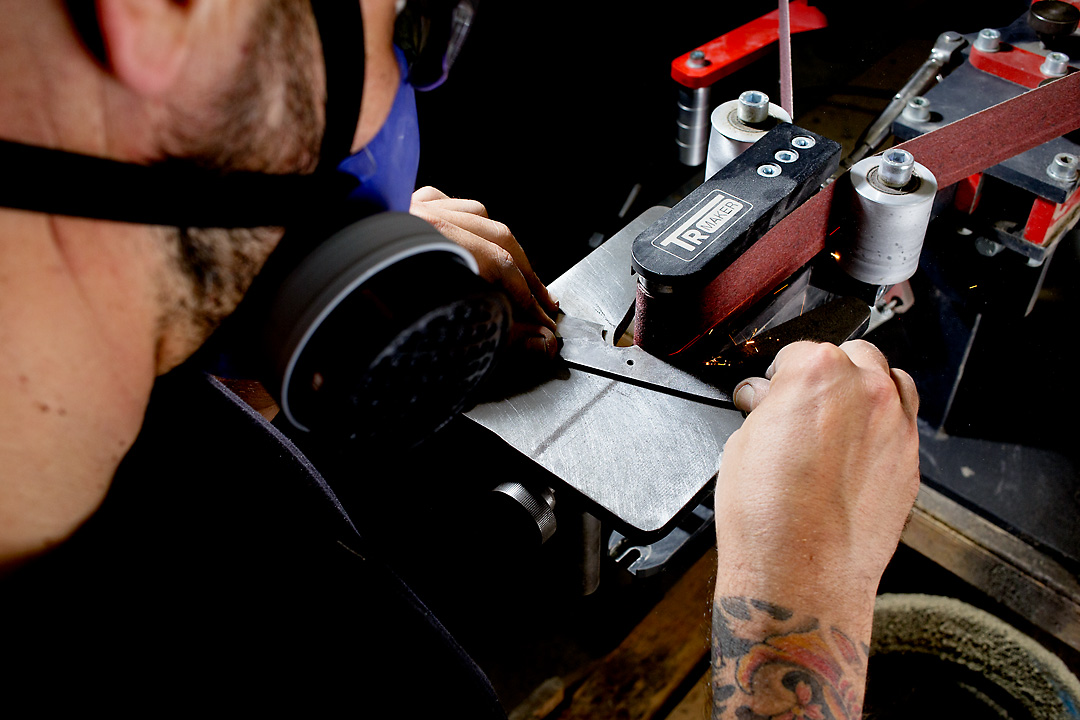 Close-up photography of a man sanding a knife from a steel sheet.