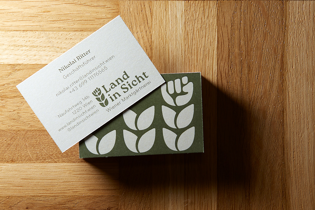 Photography of business cards for Land in Sicht. The business cards are positioned on a wooden floor and cast their shadow towards the lower right corner.