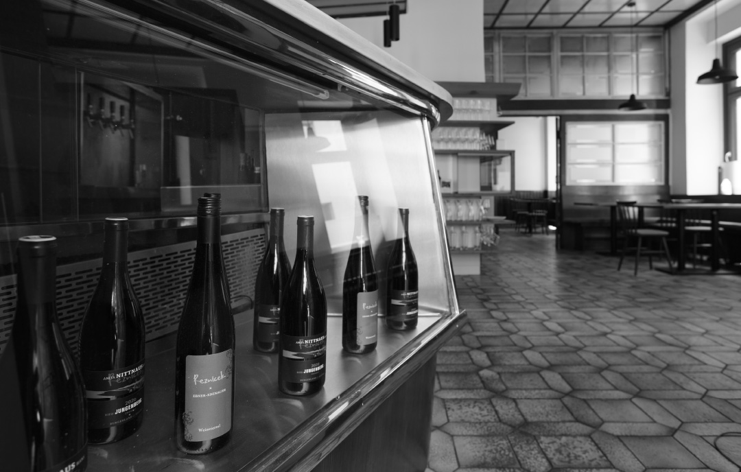 Black-and-white photography of the Reznicek restaurant in Vienna. On the left side is a vitrine which displays different wine bottles. The right side shows the inside of the restaurant from a relative low view point. This picture is used as front end-paper of a cook book designed by Koen Smet for Reznicek.