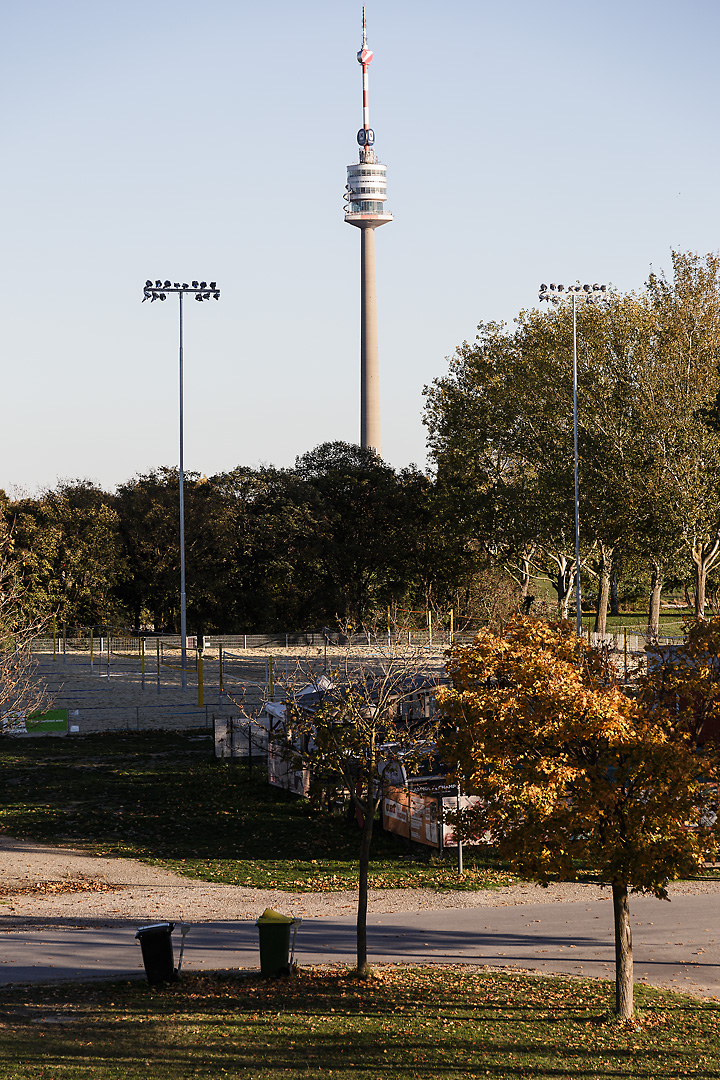 Streetphotography of the Donauturm in Vienna. On the left on right side of the tower are spotlights from a sportsfields. The scenery is set in autumn sunlight.