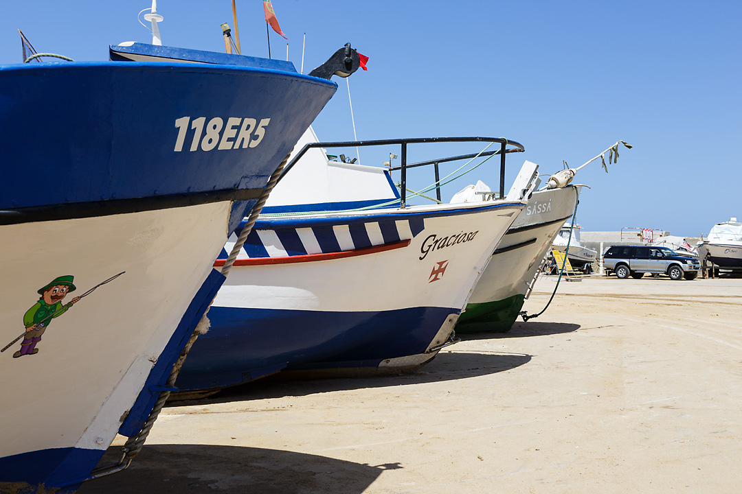 Streetphotography of the fishing harbour of Ericeira, Portugal. The bows of three fisher boats are lined up from the left. 