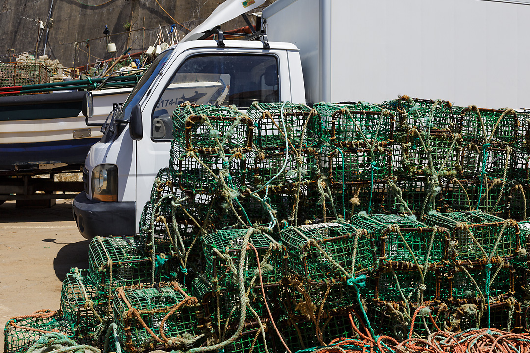 Streetphotography of the fishing harbour of Ericeira, Portugal. In front of a small white truck empty fishing cages are lined up.