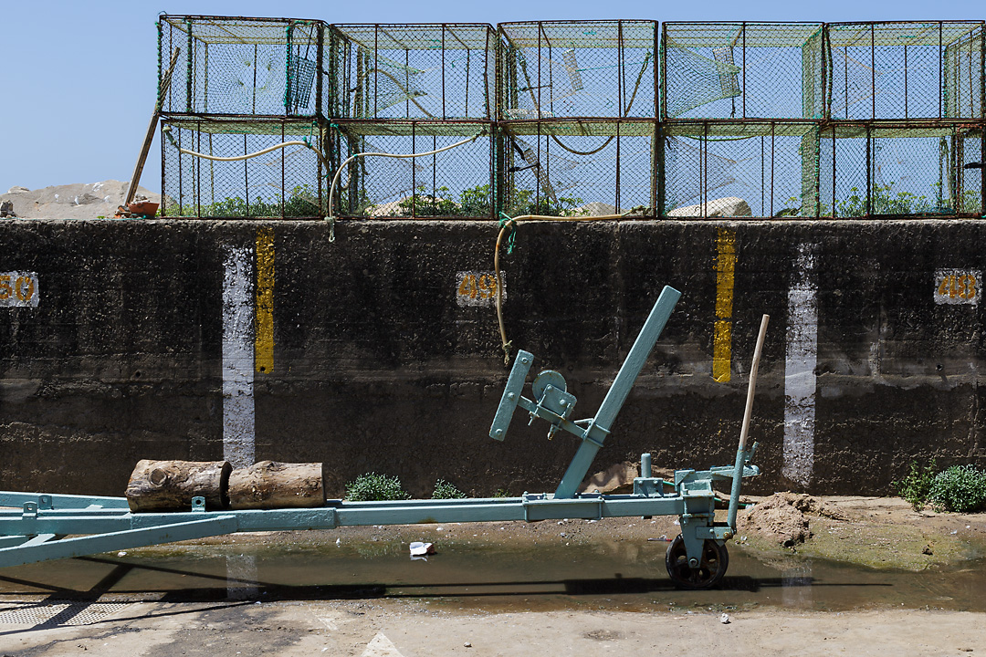 Streetphotography of the fishing harbour of Ericeira, Portugal. A frontal shot of boat towing equipment in front of a wall. On top of the wall empty fishing cages are stacked.