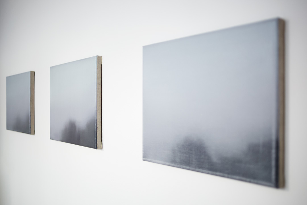 A dynamic close up of Brume V, Brume VI and Brume VII, paintings by Tom Van Puyvelde as they were displayed in the Common Sense Art Gallery in Vienna. The paintings reduce perspectively to the left, which leaves them visually wedged between two white triangles.