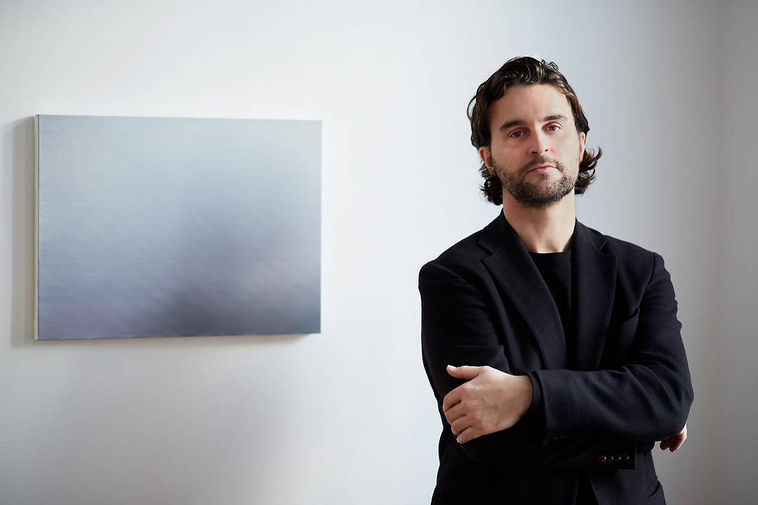 Portrait photography of the painter Tom Van Puyvelde next to his Brume IV in the Common Sense Art Gallery in Vienna. The artists is positioned on the right and has his arms crossed. He looks directly in the camera and has a serious look.