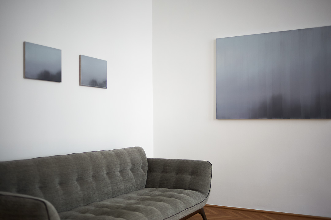 A photography of Tom Van Puyvelde's exhibition in the Common Sense Art Gallery in Vienna. The picture shows a corner with on the right wall Brume III on display and on the left wall Brume VI and Brume VII. In front a green couch is positioned against the left wall.